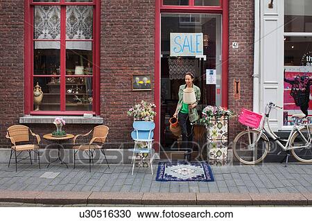 Stock Image - Young female customer with jug and lamp outside vintage shop. Fotosearch