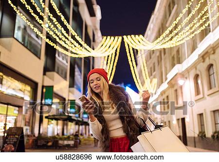 Young female shopper reading smartphone texts on street at xmas, London, UK View Large Photo Image Stock Photograph - Young female shopper reading smartphone texts on street at xmas, London, UK. Fotosearch