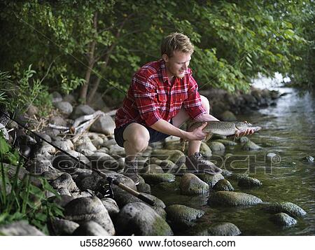 Young fisherman crouching on riverbank holding fish, Copenhagen, Denmark View Large Photo Image Stock Image - Young fisherman crouching on riverbank holding fish, Copenhagen, Denmark. Fotosearch