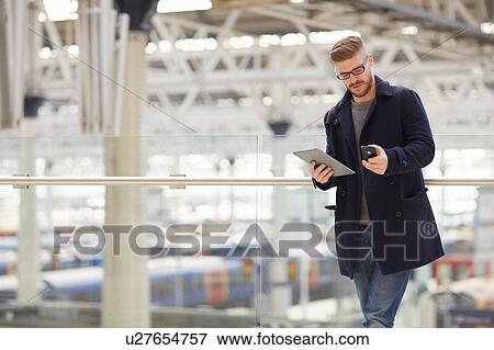 Young man at train station, holding digital tablet and smartphone View Large Photo Image Stock Photo - Young man at train station, holding digital tablet and smartphone. Fotosearch