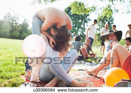 Picture - Young man bending forward to kiss girlfriend at park party. Fotosearch