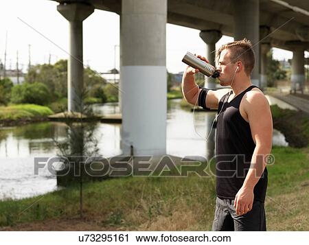 Young man beside river, drinking from water bottle View Large Photo Image Stock Image - Young man beside river, drinking from water bottle. Fotosearch