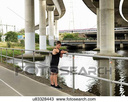 Young man beside river, leaning on railings, using MP3 player attached to arm View Large Photo Image Stock Image - Young man beside river, leaning on railings, using MP3 player attached to arm. Fotosearch