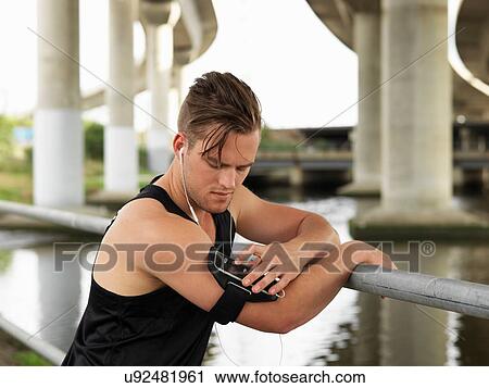 Young man beside river, leaning on railings, using MP3 player attached to arm View Large Photo Image Stock Image - Young man beside river, leaning on railings, using MP3 player attached to arm. Fotosearch