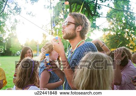 Young man blowing bubbles at group party in park at sunset View Large Photo Image Stock Photo - Young man blowing bubbles at group party in park at sunset. Fotosearch