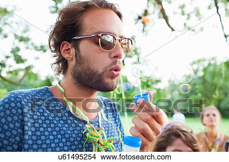 Young man blowing bubbles at sunset party in park View Large Photo Image Picture - Young man blowing bubbles at sunset party in park. Fotosearch