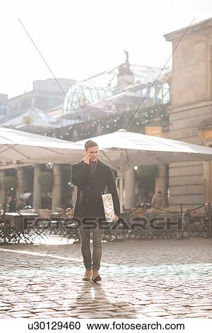 Stock Image - Young man carrying gift and chatting on smartphone in Covent Garden, London, UK. Fotosearch
