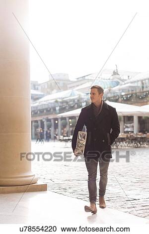 Stock Image - Young man carrying gift in Covent Garden, London, UK. Fotosearch