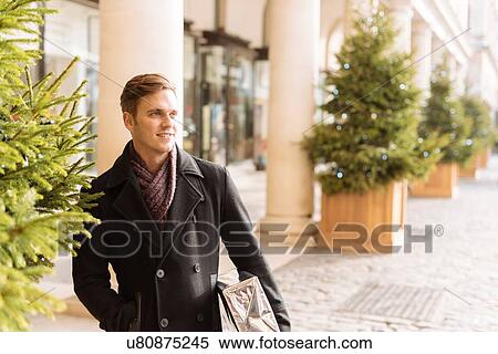 Stock Photography - Young man carrying xmas gift standing in Covent Garden, London, UK. Fotosearch
