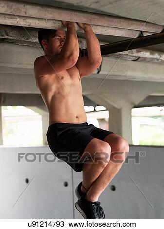Stock Image - Young man doing pull ups under bridge. Fotosearch