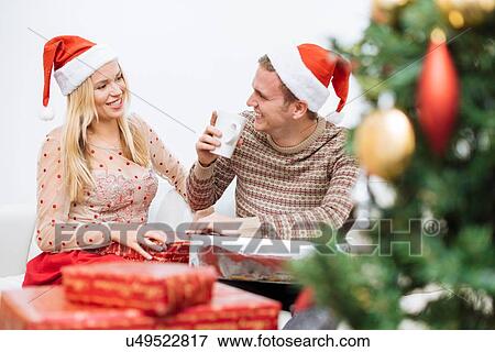 Stock Photo - Young man drinking coffee with girlfriend surrounded by christmas presents. Fotosearch