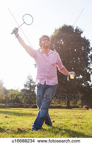 Young man drinking whilst playing badminton in sunlit park View Large Photo Image Picture - Young man drinking whilst playing badminton in sunlit park. Fotosearch