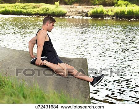 Young man exercising beside river, stretching leg View Large Photo Image Picture - Young man exercising beside river, stretching leg. Fotosearch
