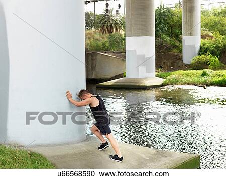 Young man exercising beside river, leaning against column, stretching View Large Photo Image Stock Image - Young man exercising beside river, leaning against column, stretching. Fotosearch