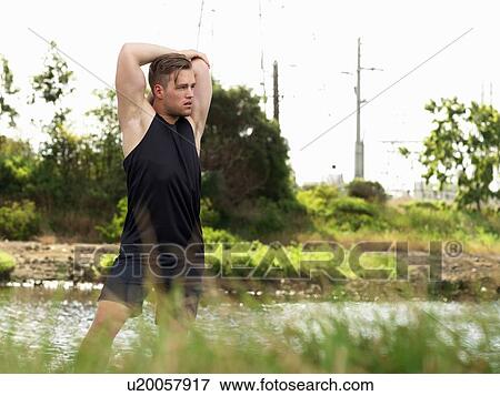 Young man exercising beside river, stretching arms View Large Photo Image Stock Photo - Young man exercising beside river, stretching arms. Fotosearch