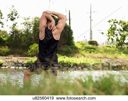 Young man exercising beside river, stretching arms, rear view View Large Photo Image Stock Photo - Young man exercising beside river, stretching arms, rear view. Fotosearch