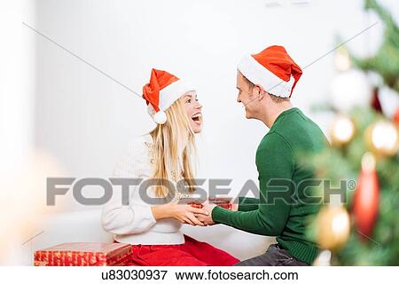 Stock Photo - Young man handing christmas present to happy girlfriend. Fotosearch