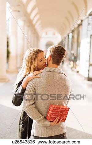 Stock Photograph - Young man hiding xmas gift for girlfriend in Covent Garden, London, UK. Fotosearch