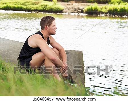 Stock Photo - Young man in sports sitting on riverbank. Fotosearch