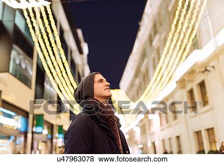 Stock Photo - Young man looking up at xmas lights, London, UK. Fotosearch