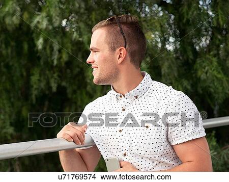 Young man, outdoors, leaning on railings, looking away View Large Photo Image Picture - Young man, outdoors, leaning on railings, looking away. Fotosearch
