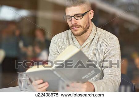 Young man sitting in cafe, reading book View Large Photo Image Stock Photography - Young man sitting in cafe, reading book. Fotosearch