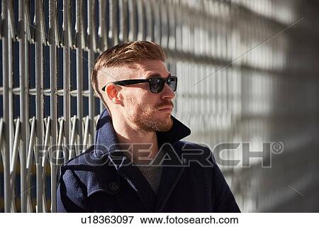 Young man standing beside metal fence, pensive expression View Large Photo Image Stock Photo - Young man standing beside metal fence, pensive expression. Fotosearch