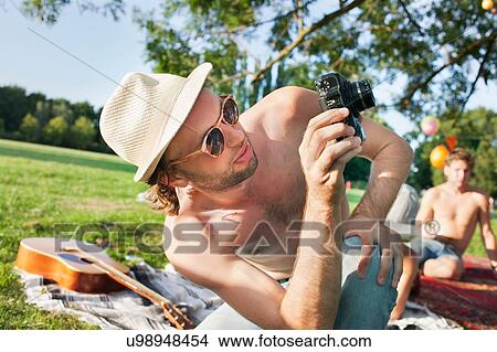 Picture - Young man taking photographs at park party. Fotosearch