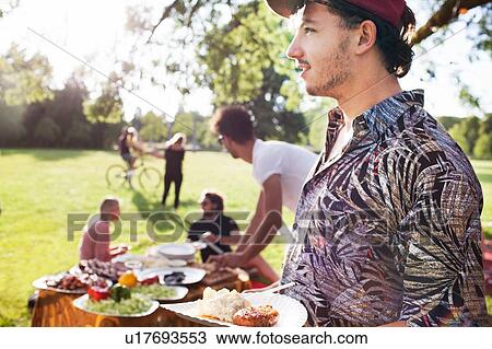 Young man with plate of picnic food at park party View Large Photo Image Stock Image - Young man with plate of picnic food at park party. Fotosearch