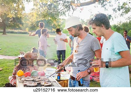 Stock Photograph - Young men barbecuing at group party in park. Fotosearch