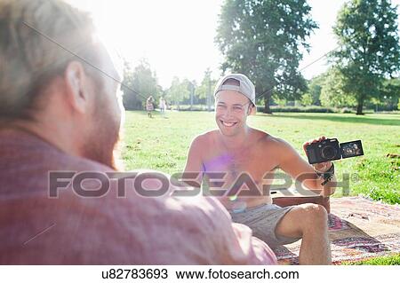 Stock Image - Young men reviewing photographs on camera at park party. Fotosearch