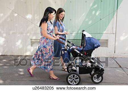 Stock Photography - Young woman and mother and pushing baby carriage along street. Fotosearch