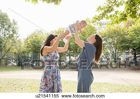 Stock Photography - Young woman and mother holding up baby girl in park. Fotosearch