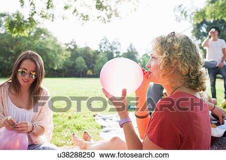Young woman blowing up balloon at park party View Large Photo Image Stock Image - Young woman blowing up balloon at park party. Fotosearch