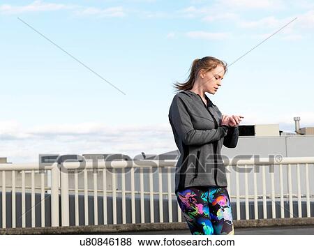 Young woman checking watch whilst training in parking lot View Large Photo Image Stock Photo - Young woman checking watch whilst training in parking lot. Fotosearch