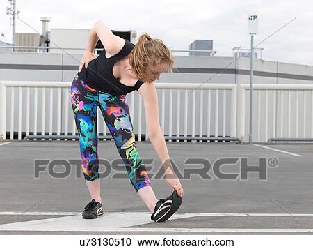 Stock Image - Young woman doing stretch training in parking lot. Fotosearch