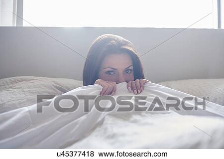 Stock Photo - Young woman hiding under bed covers. Fotosearch