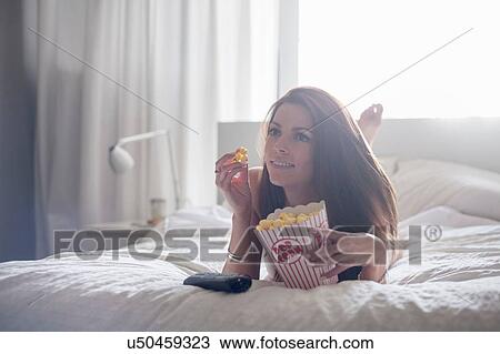 Young woman lying on bed, eating popcorn View Large Photo Image Stock Image - Young woman lying on bed, eating popcorn. Fotosearch