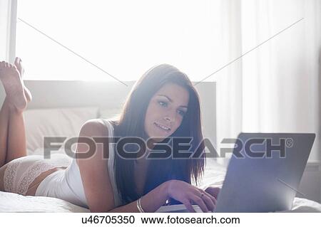 Young woman lying on bed, using laptop View Large Photo Image Stock Image - Young woman lying on bed, using laptop. Fotosearch