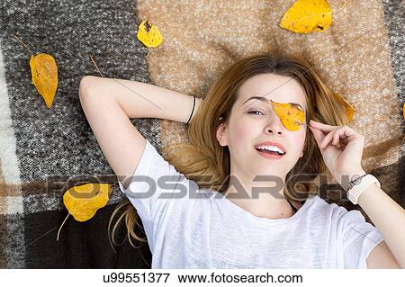 Stock Photo - Young woman lying on blanket, covering eye with leaf. Fotosearch