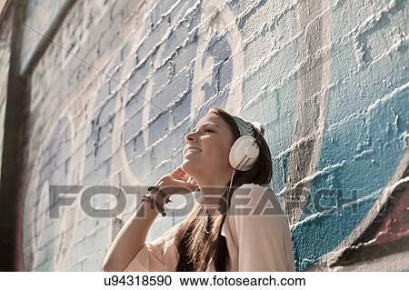 Young woman outdoors, listening to music through headphones View Large Photo Image Stock Image - Young woman outdoors, listening to music through headphones. Fotosearch