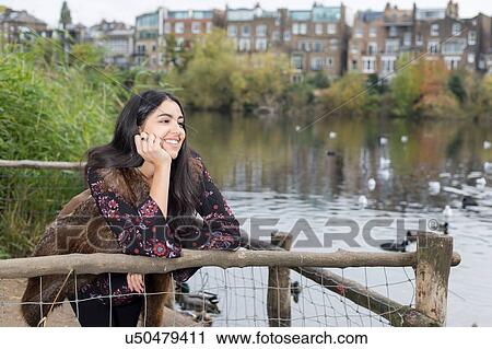 Stock Image - Young woman relaxing by lake, Hampstead Heath, London. Fotosearch