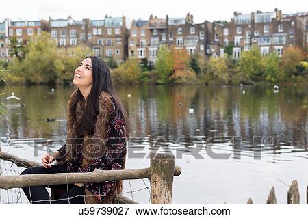 Stock Photo - Young woman relaxing by lake, Hampstead Heath, London. Fotosearch