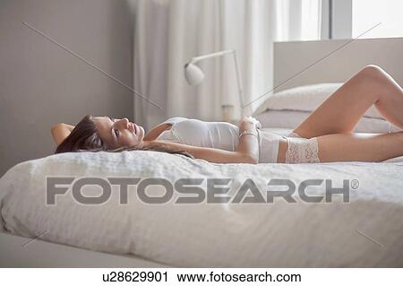 Stock Image - Young woman relaxing in bed. Fotosearch