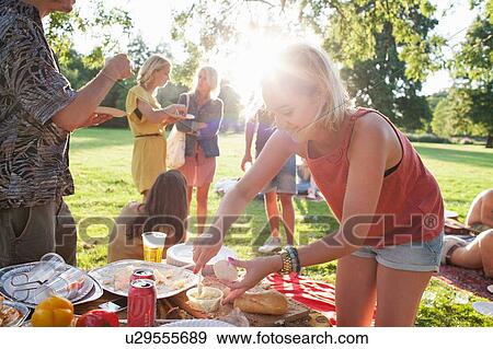 Stock Photo - Young woman selecting food at group party picnic in park. Fotosearch