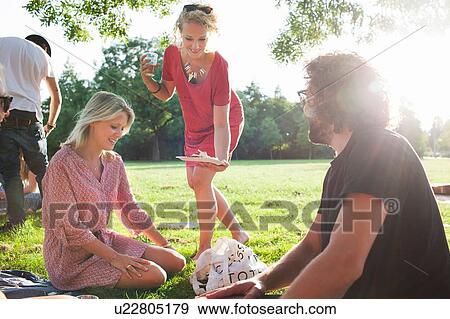 Stock Photo - Young woman sharing food at sunset park party. Fotosearch