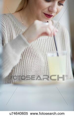 Stock Photography - Young woman sitting in cafe, drinking cold drink. Fotosearch