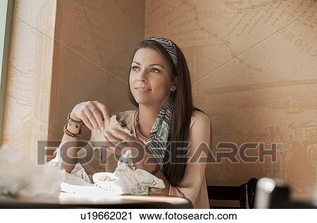 Young woman sitting in cafe, eating sandwich View Large Photo Image Stock Image - Young woman sitting in cafe, eating sandwich. Fotosearch