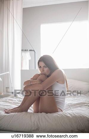 Young woman sitting on bed, hugging knees View Large Photo Image Stock Photo - Young woman sitting on bed, hugging knees. Fotosearch