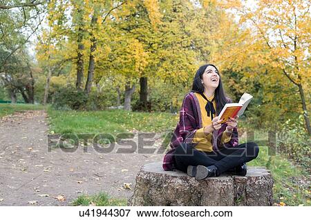 Stock Photo - Young woman with book on tree stump, Hampstead Heath, London. Fotosearch